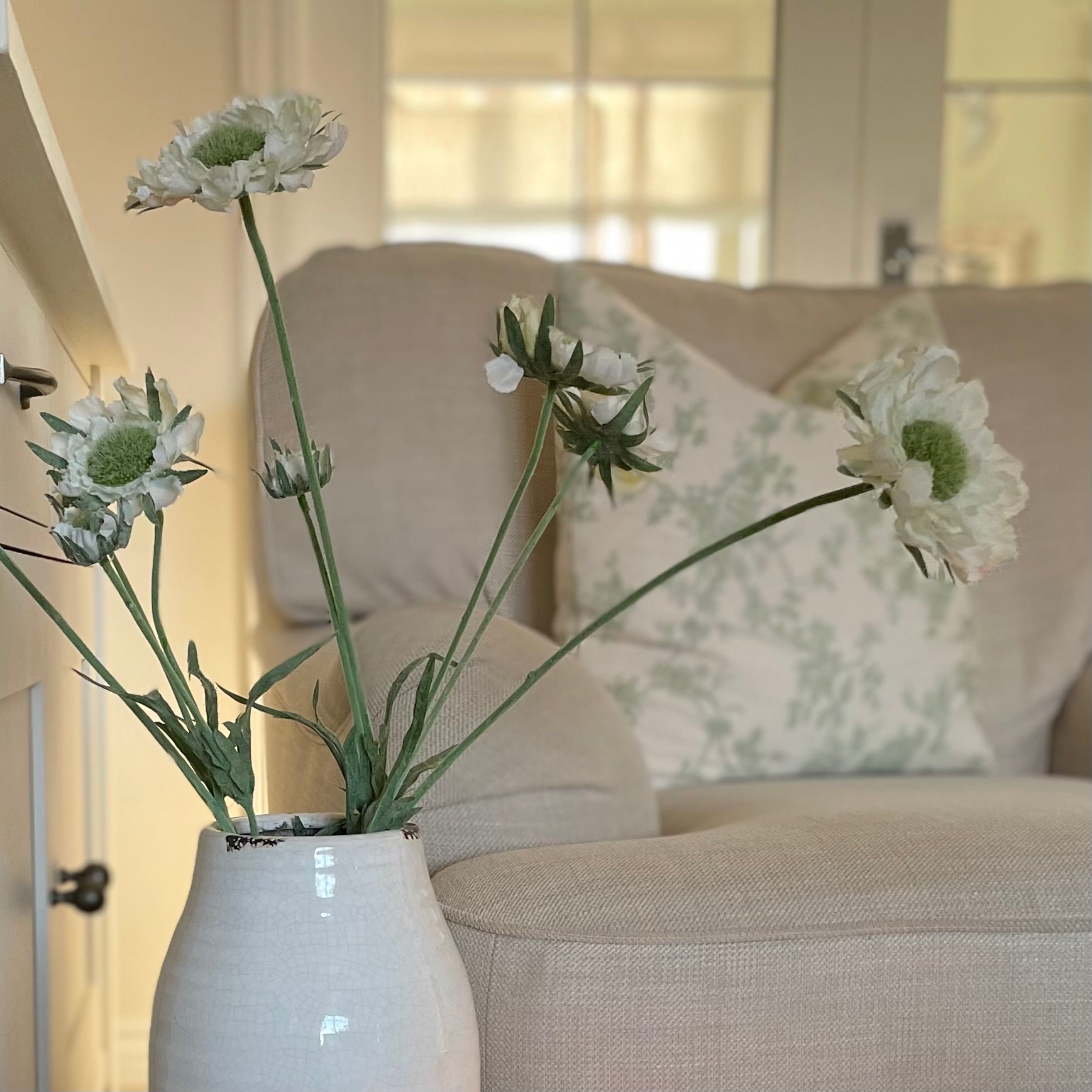 Close up of Faux Scabiosa Stem with off white flowers and soft green centres, styled in a Stephanie glazed vase. Styled in a cosy living room.