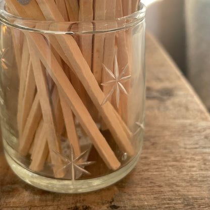Glass match pot with etched star detail, grey matches, and hidden striker pad on the base. Styled on a wooden rustic stool.