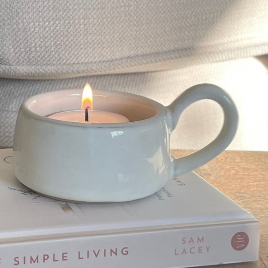 White ceramic tea light holder with handle, styled on a wooden table and book or a cosy home look.