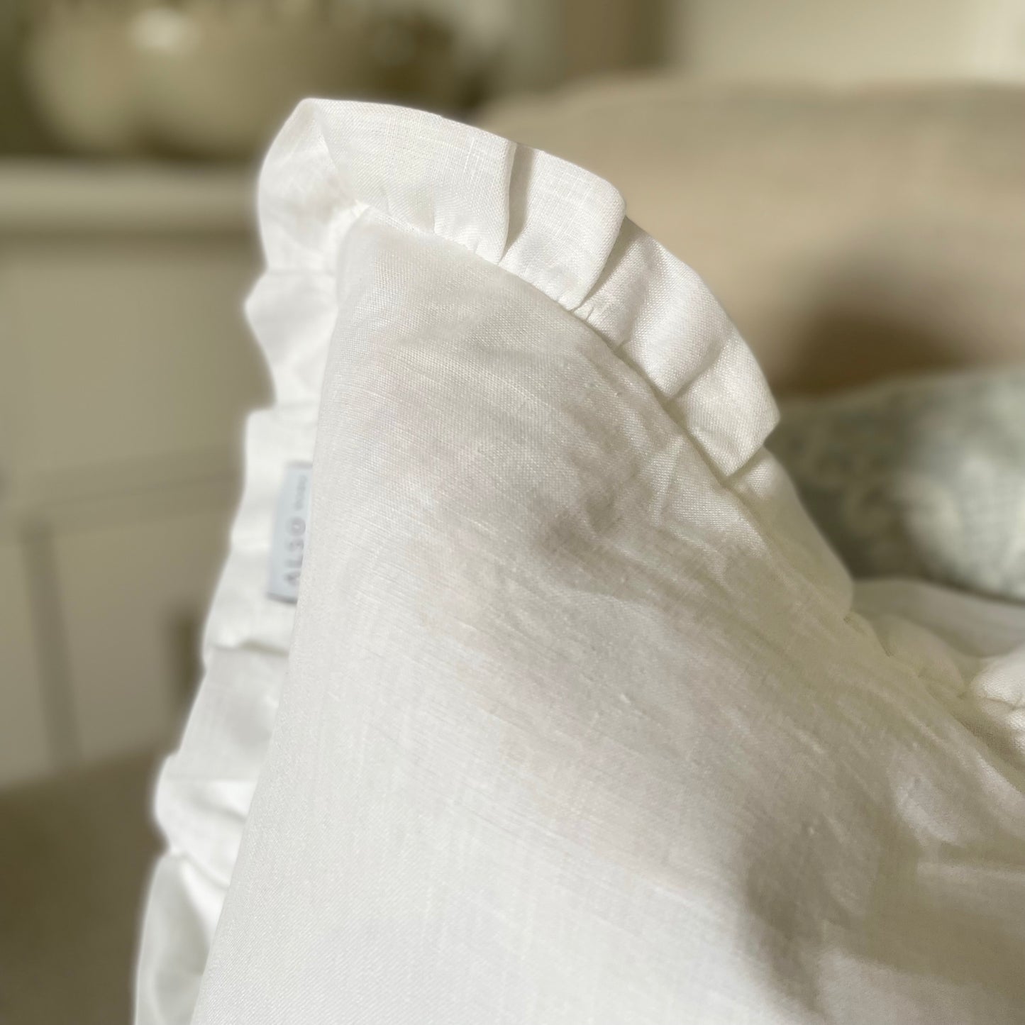 White linen cushion with ruffled edge and mother of pearl button detail styled on a sofa.