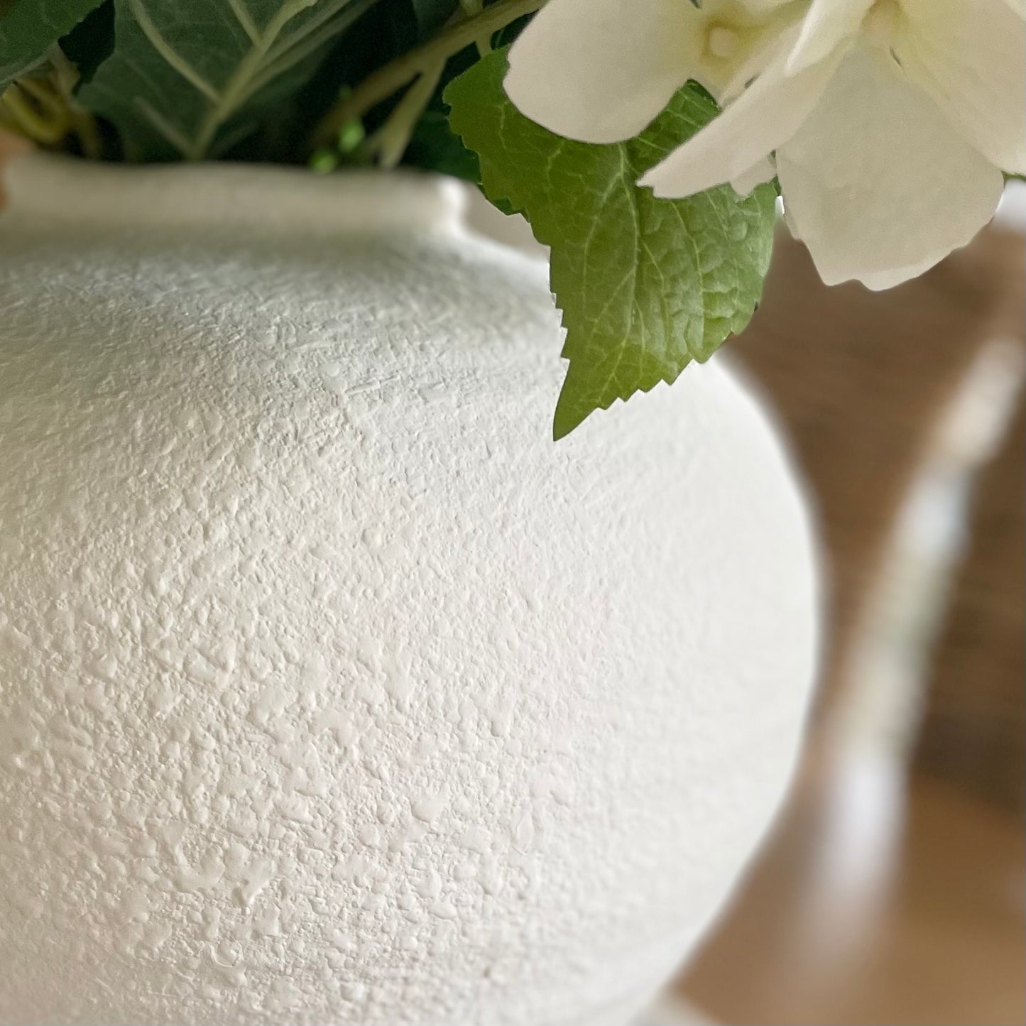 White matte roman urn style Regola vase with soft textured finish and elegant curved shape. Styled with a white hydrangea bouquet.