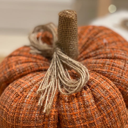 Knitted pumpkin with rustic hessian stalk styled on a wooden floor with autumn foliage.