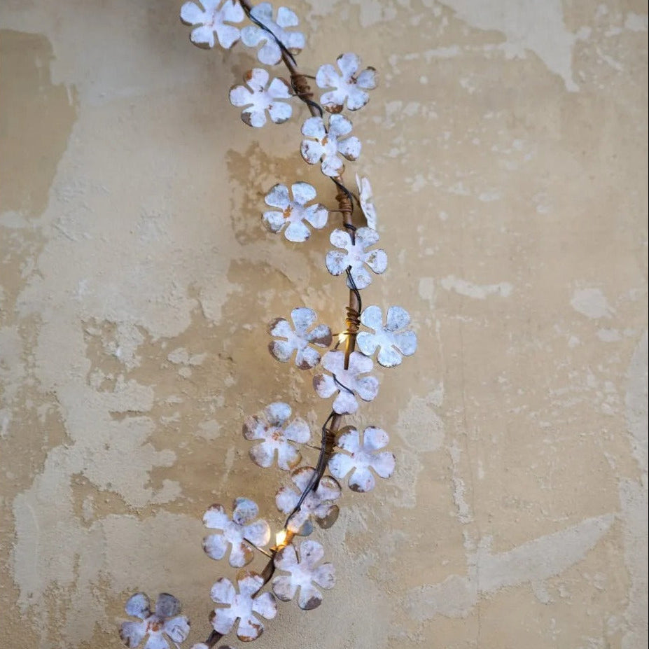 Dainty wildflower wreath with faded white leaves and warm white LED lights, hanging on a rustic wall.
