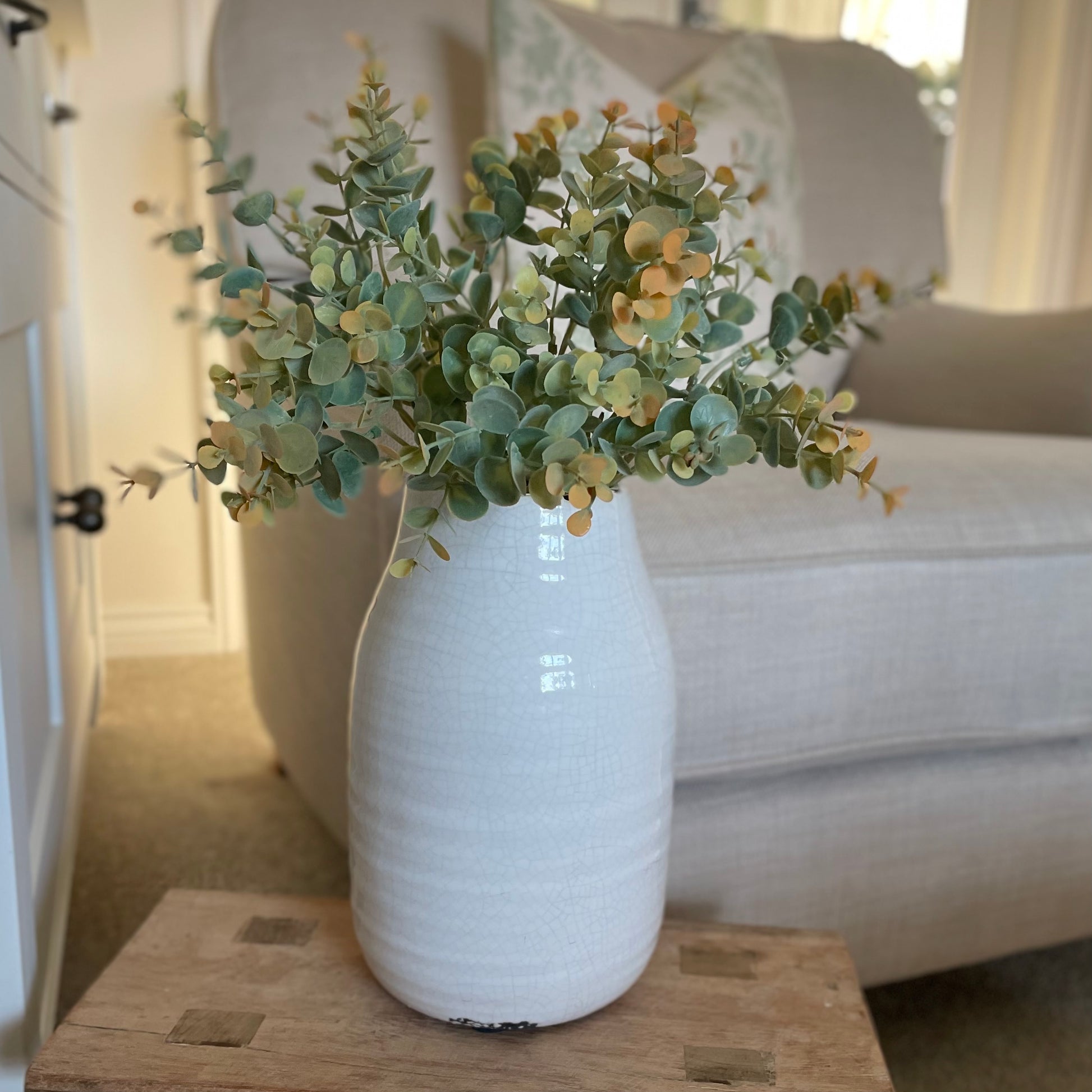 Cream crackle glazed ceramic vase with textured finish, ideal for short faux stems. Styled in a living room on a wooden stool.