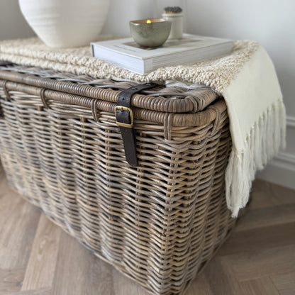 Wicker storage basket with a blanket draped over it on a wooden floor.