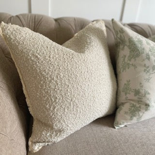 Textured soft cream boucle cushion with fringe detailing, styled in a neutral living room.