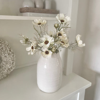 Faux cosmos floral spray styled in a ceramic glazed vase on a console table.
