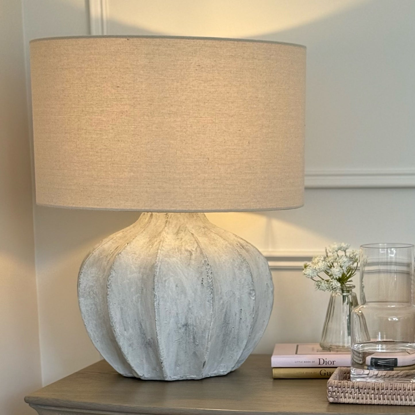 Table lamp with textured base and beige shade on a nightstand.