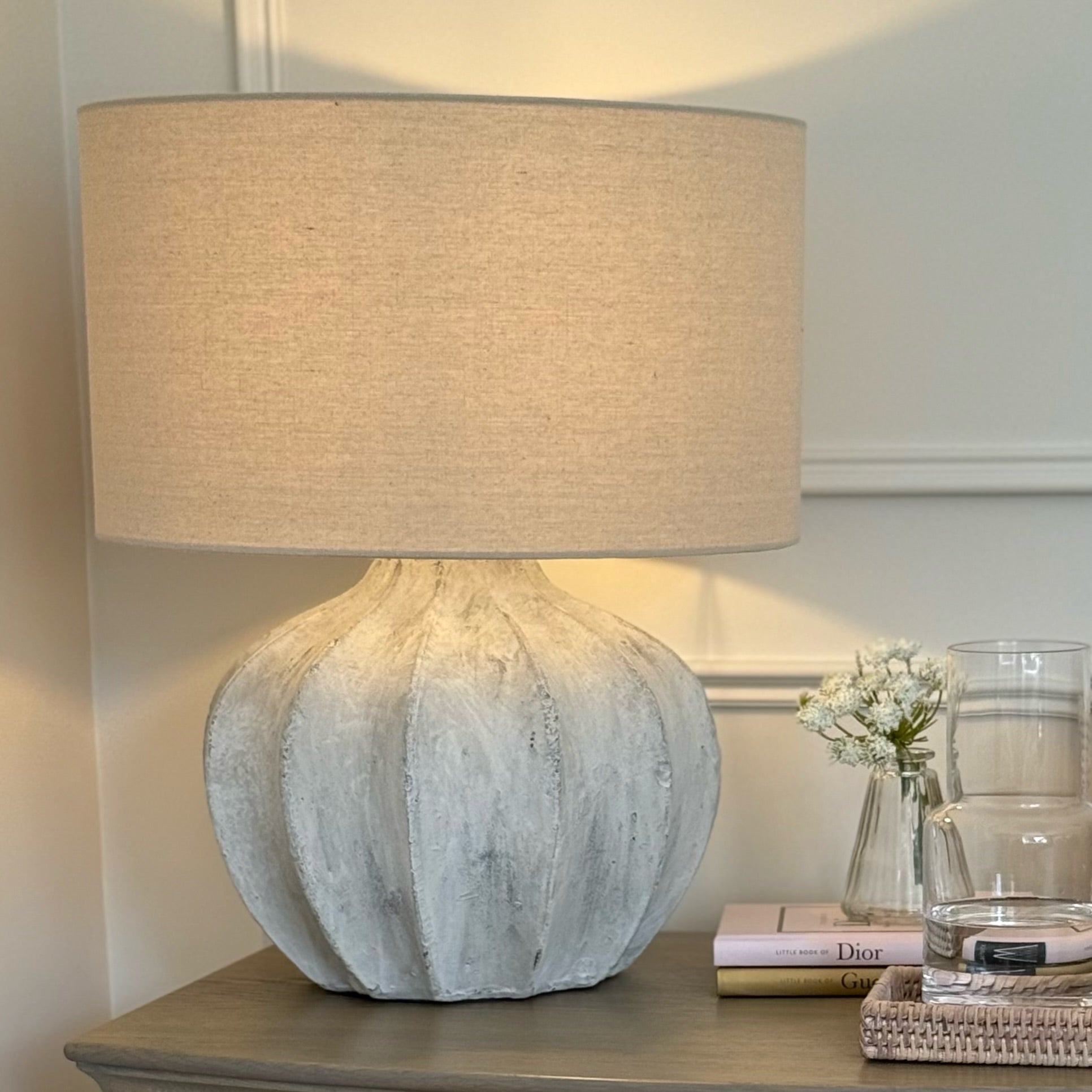 Table lamp with textured base and beige shade on a nightstand.