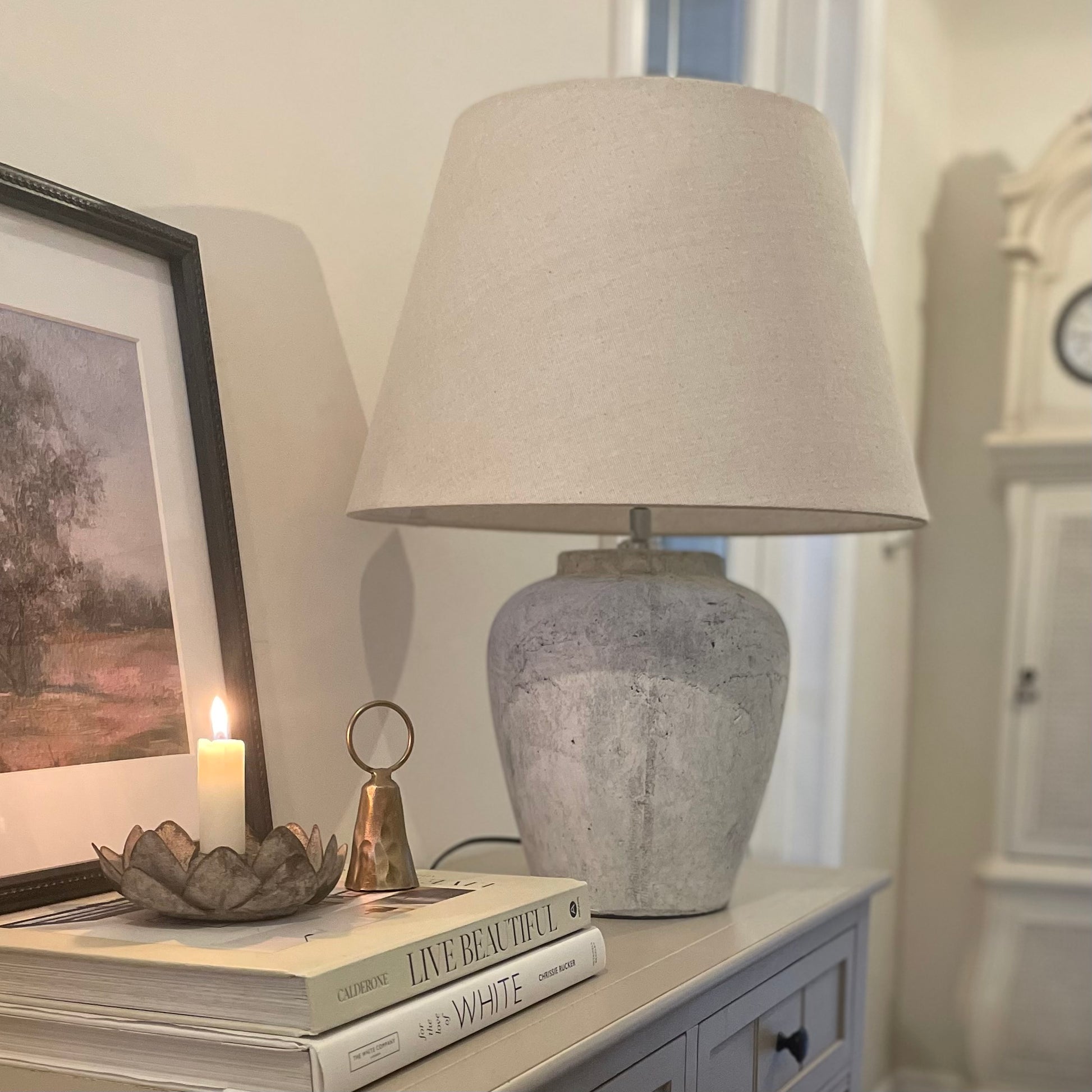 Darcy lamp with neutral stone base and linen hat shade. Styled on a console table with a candle in a neutral hallway.