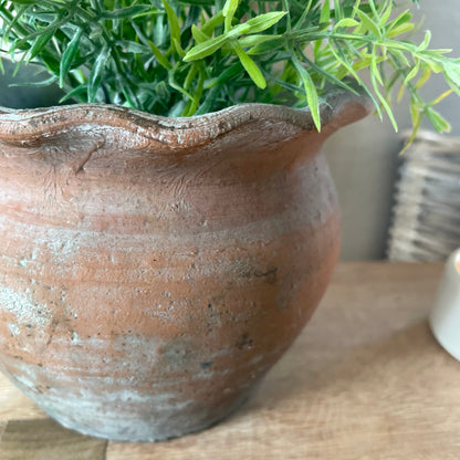 Close up of handcrafted terracotta pie crust pot, styled with a faux plant on a rustic wooden stool.