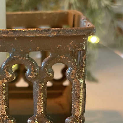 Close up of softly distressed tin candle holder with candles lit. Styled in front of garland with lights.