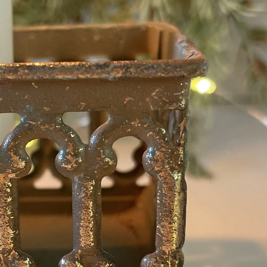 Close up of softly distressed tin candle holder with candles lit. Styled in front of garland with lights.