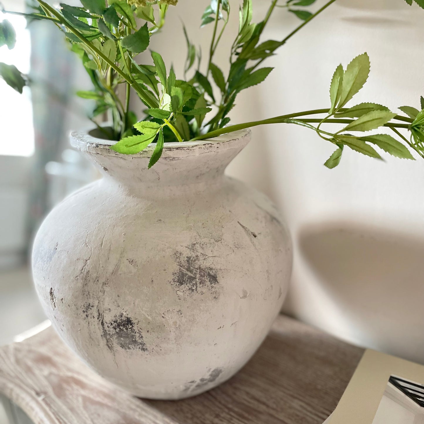 White distressed vase with greenery on a wooden console table.