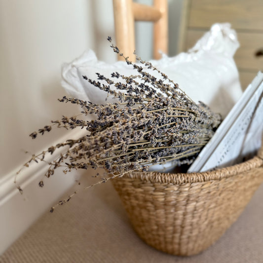 Dried lavender bunch wrapped styled in seagrass shopper with a cushion and book.