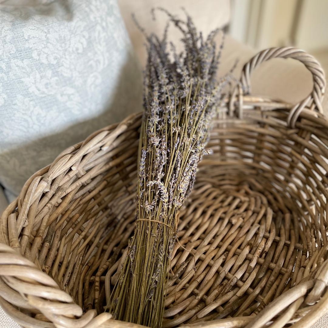 Dried lavender bunch wrapped in brown paper and tied with jute string, styled on a rattan basket.