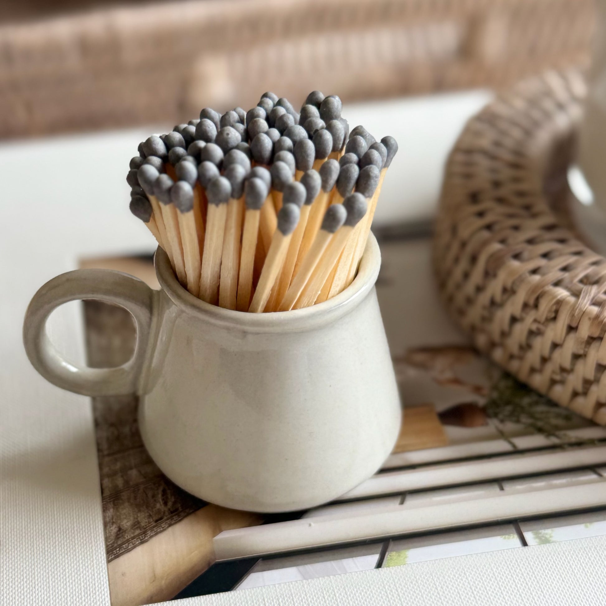 Matches in a ceramic cup on a table with a wicker basket in the background