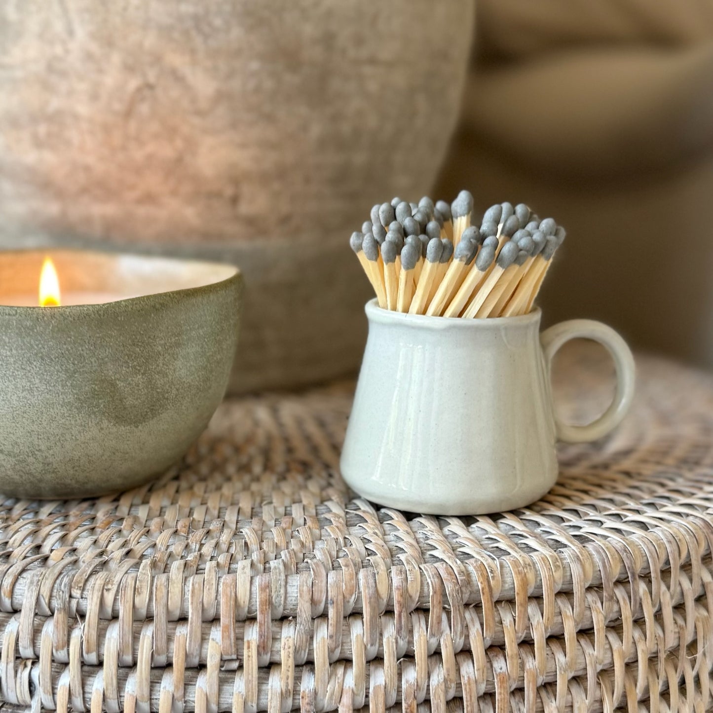 Matches in a small ceramic cup next to a lit candle on a woven surface