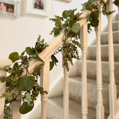 Realistic eucalyptus garland draped on a white staircase banister.