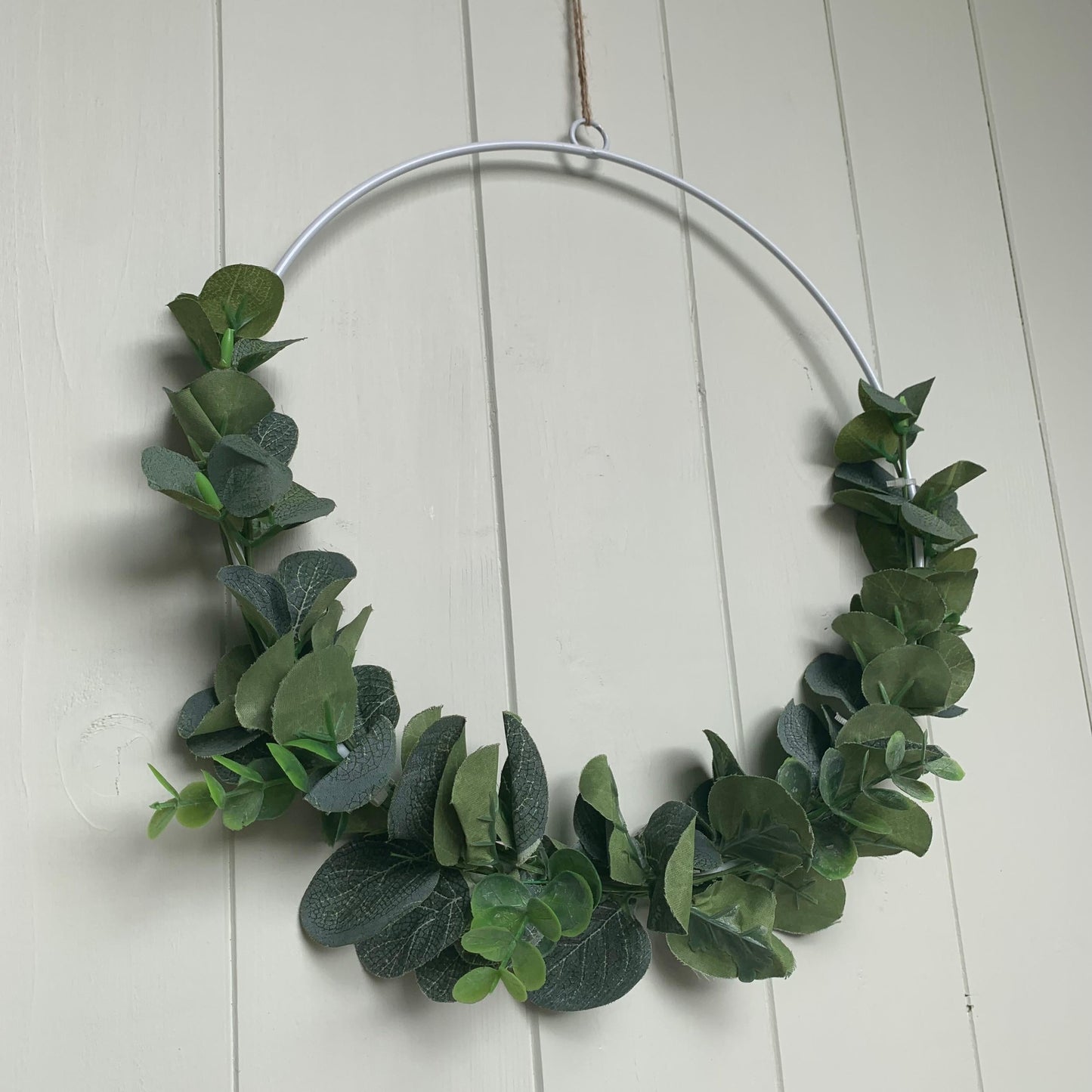 White metal wreath decorated with artificial eucalyptus and hanging on a door with jute string.