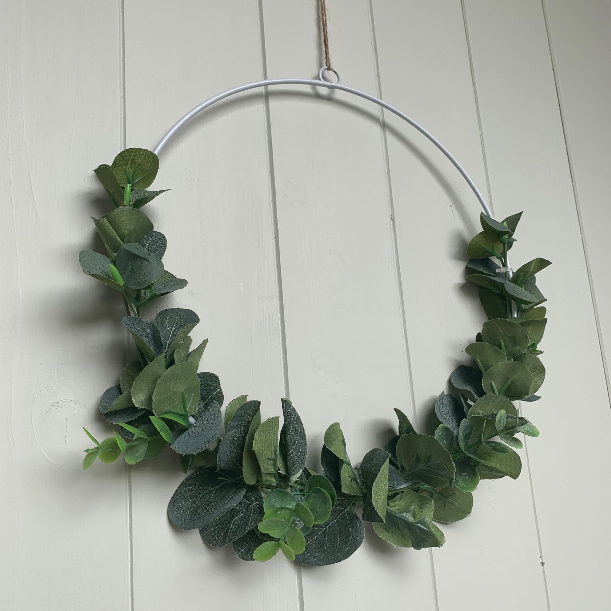 White metal wreath decorated with artificial eucalyptus and hanging on a door with jute string.