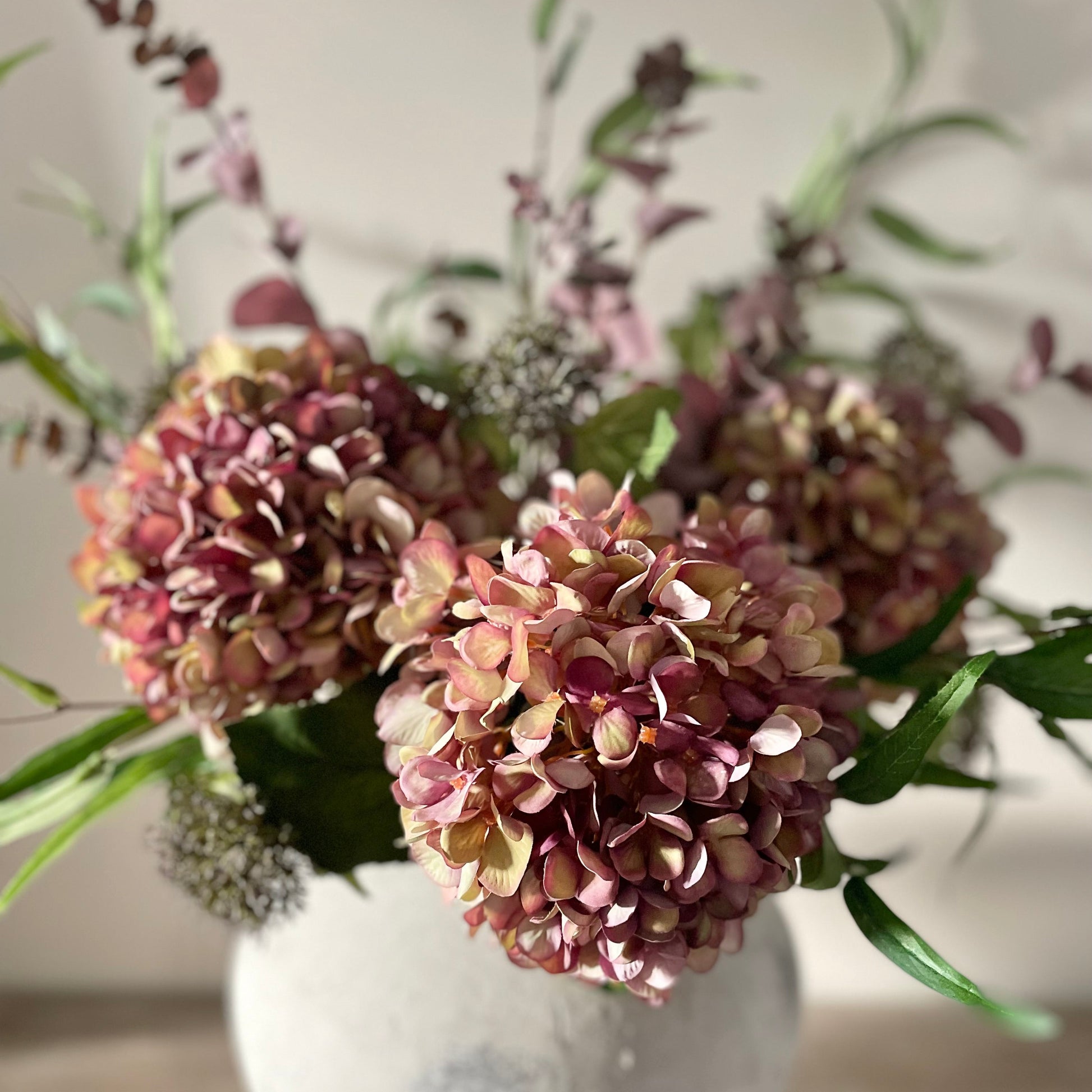 Autumn bouquet of faux flowers in a stone vase on a wooden table with a blurred background