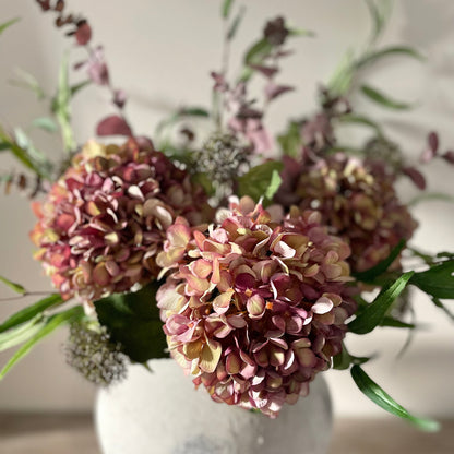 Autumn bouquet of faux flowers in a stone vase on a wooden table with a blurred background
