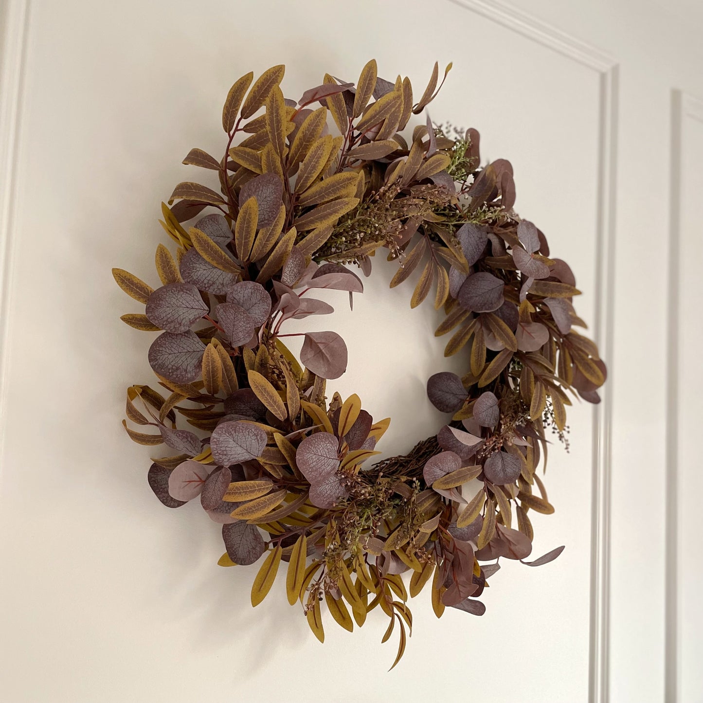 Full autumn foliage wreath with rich fall colours, styled as door or wall decor. Styled on a white panelled wall