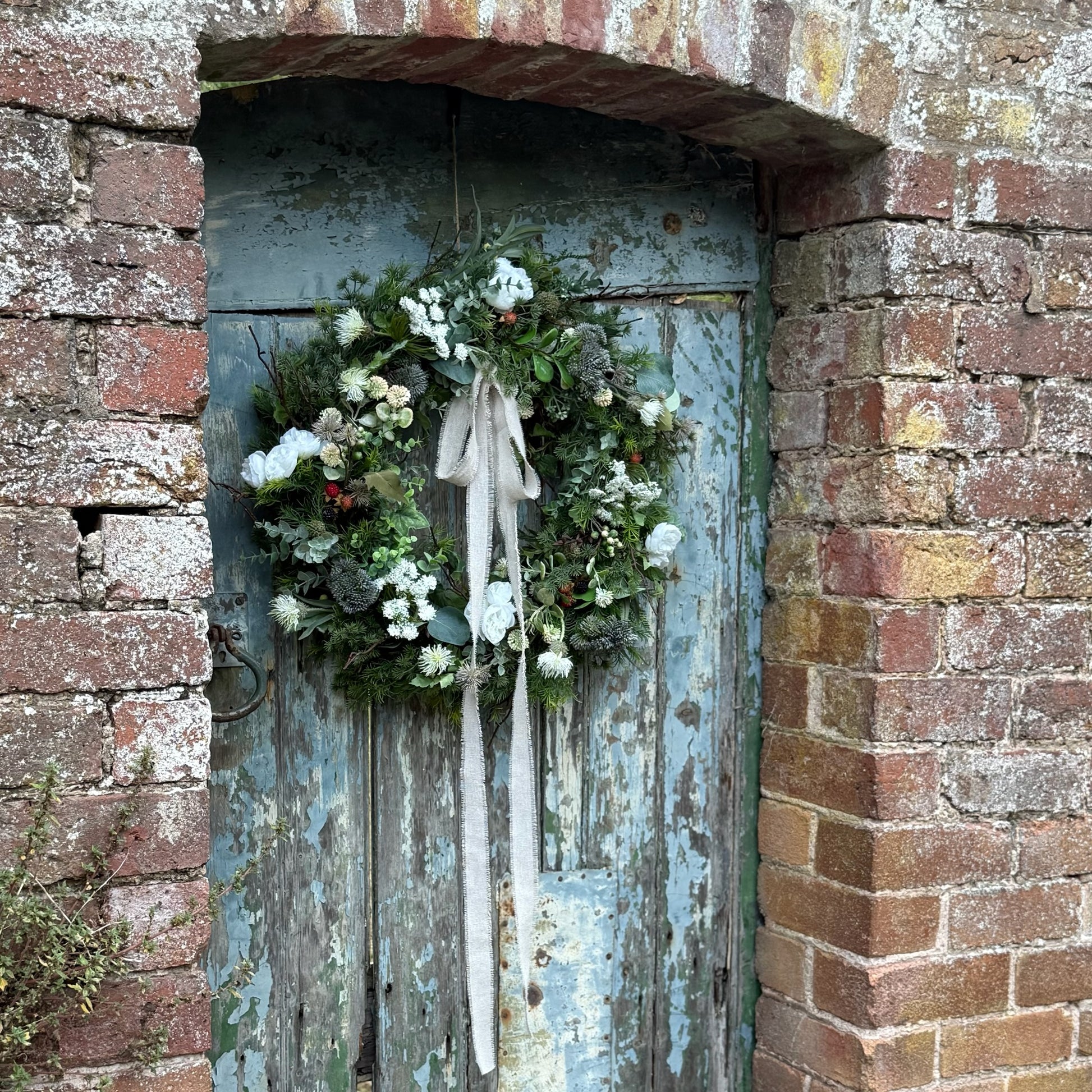 Faux bramble wreath on a rustic wooden door with brick wall background.