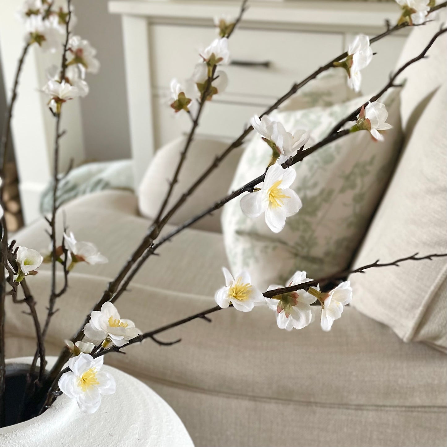 Faux cherry blossom branch with delicate white flowers and yellow pistils.