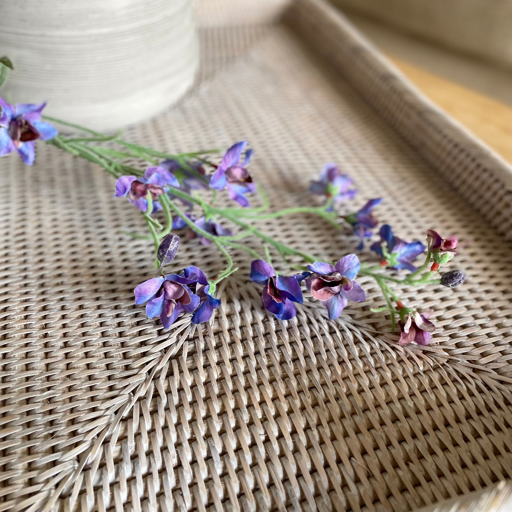 Faux blue and purple delphinium spray, 76 cm tall, styled on a rattan tray.