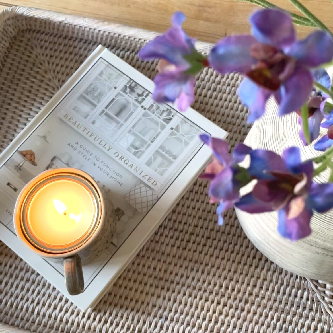 Faux blue and purple delphinium spray, 76 cm tall, styled in a stone vase on a rattan tray with a candle lit.