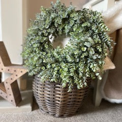 Decorative eucalyptus flocked wreath in a woven basket.