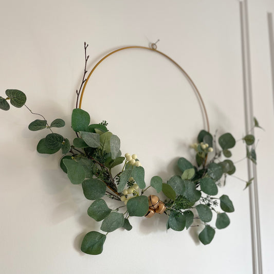 Gold metal ring wreath with eucalyptus foliage and white berries. Styled on w white panelled wall.
