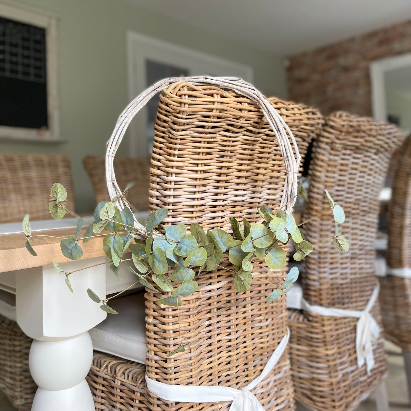 Beautiful faux eucalyptus wreath on a twig frame. Hanging on a wicker rustic dining room chair.