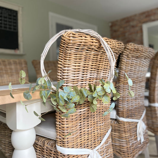 Beautiful faux eucalyptus wreath on a twig frame. Hanging on a wicker rustic dining room chair.