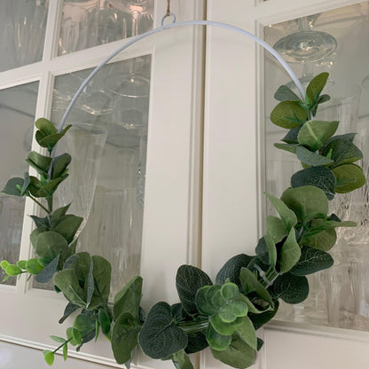 White metal wreath decorated with artificial eucalyptus and hanging on a door with jute string.