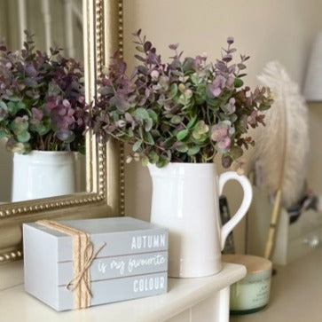 Artificial eucalyptus spray with soft green and burgundy tinted leaves styled in a rustic white vase on a wooden table, adding a subtle autumnal touch to the home.