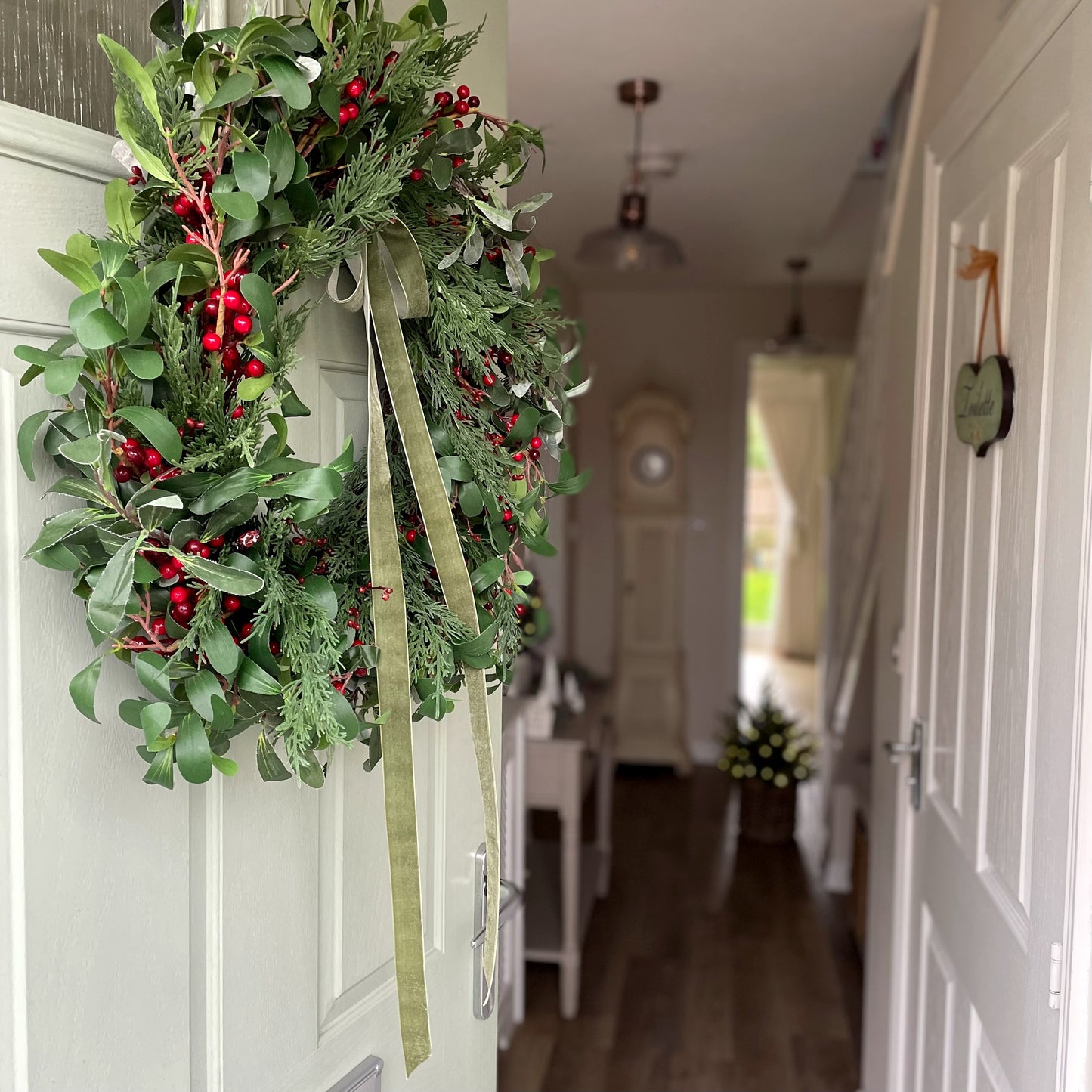 Festive faux fir and red berry wreath styled on a front door. Showing other christmas decor in a cosy hallway.