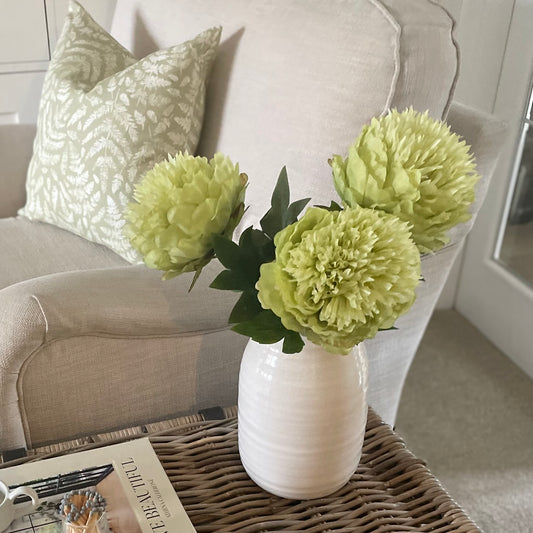 Faux garden peony stem with bright green bloom and leaves, styled on a wicker coffee table in a cosy living room.