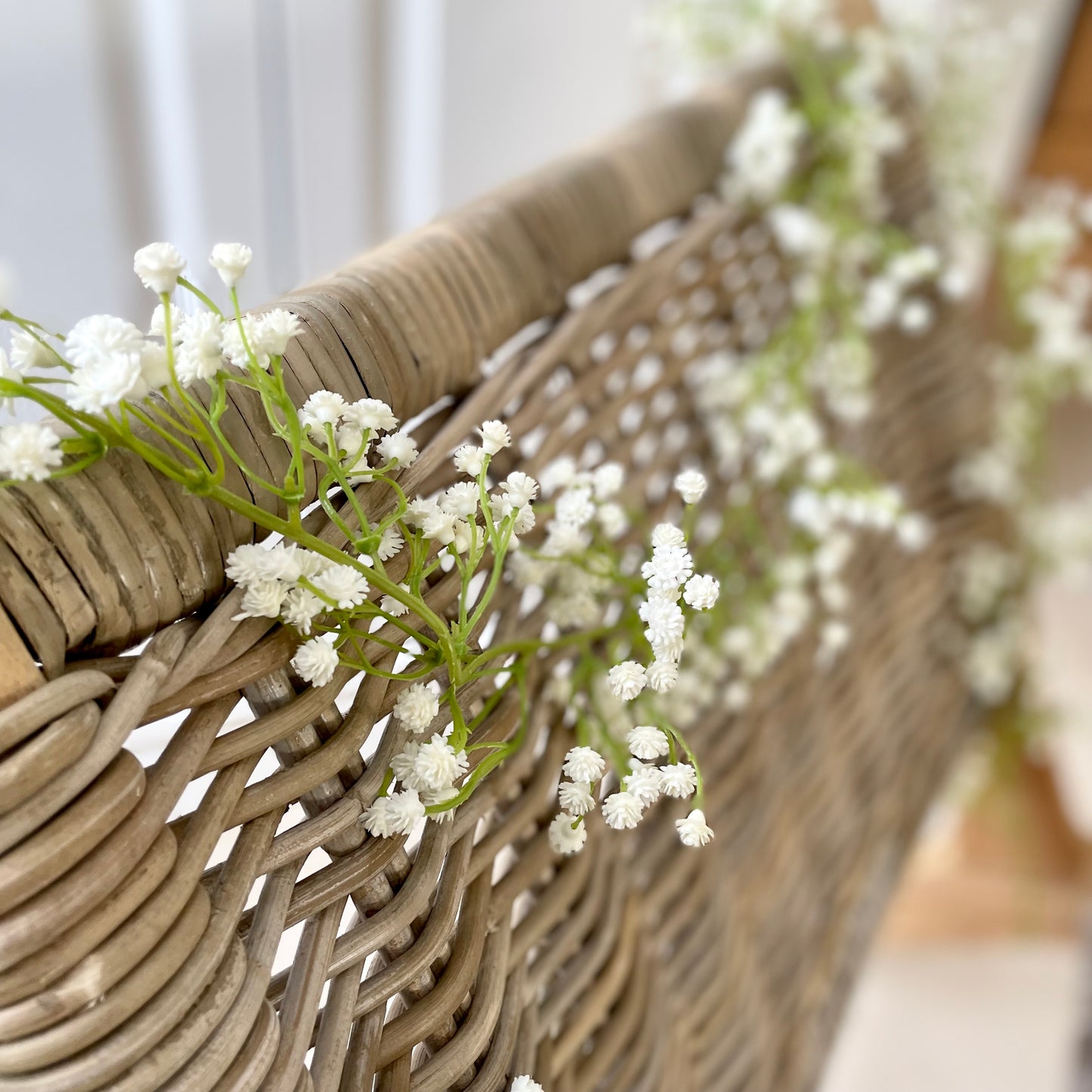 White faux gypsophila flower garland draped on a rattan chair.