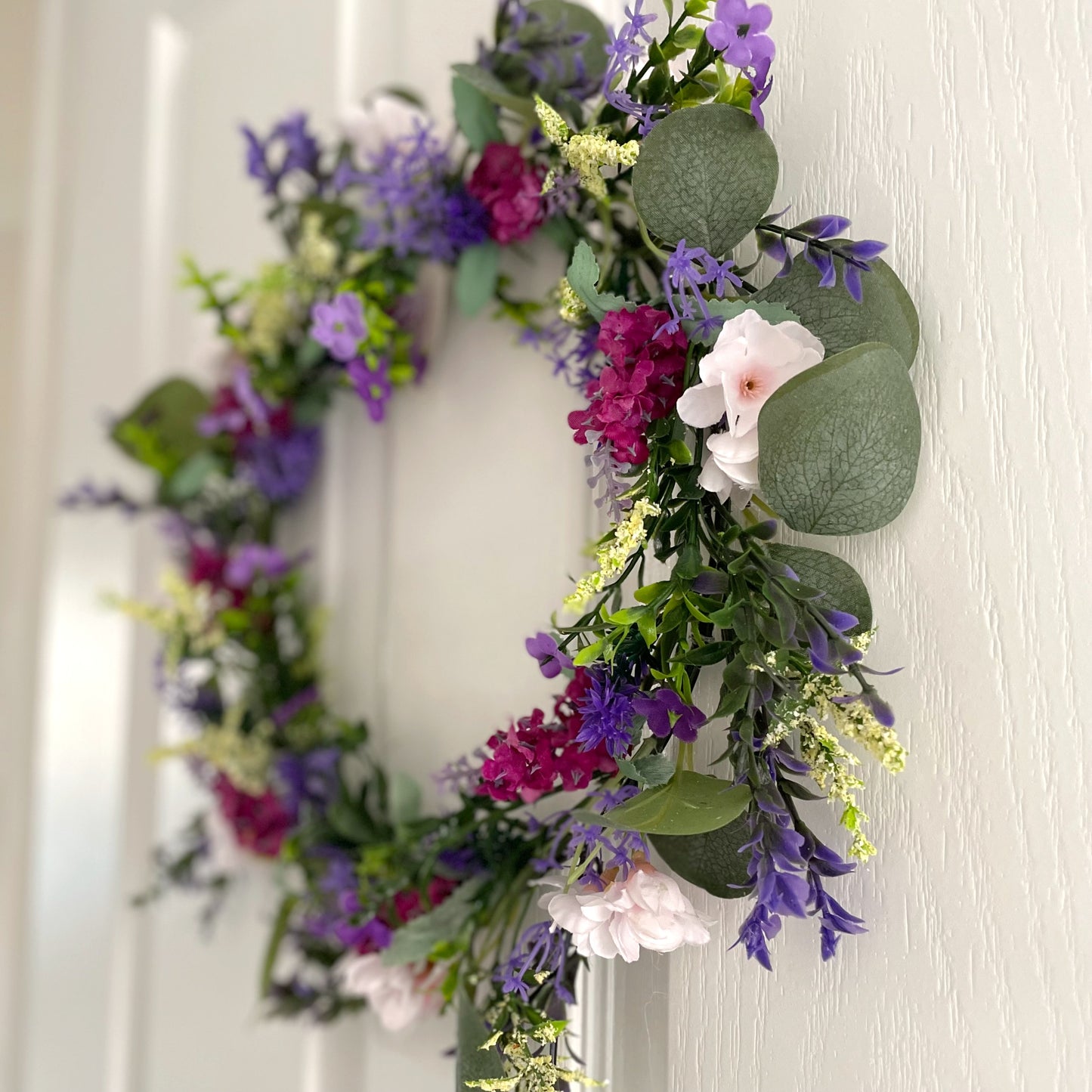 Faux lavender wreath with purple and white blooms, eucalyptus and peach wildflowers, 40 cm diameter styled on a white door.
