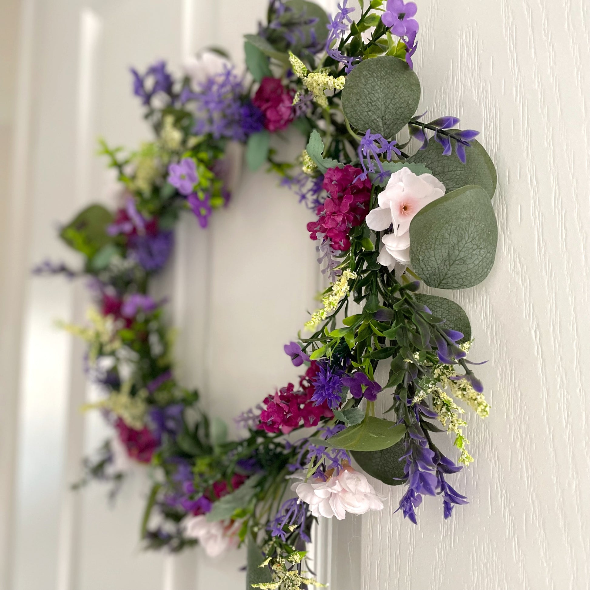 Faux lavender wreath with purple and white blooms, eucalyptus and peach wildflowers, 40 cm diameter styled on a white door.