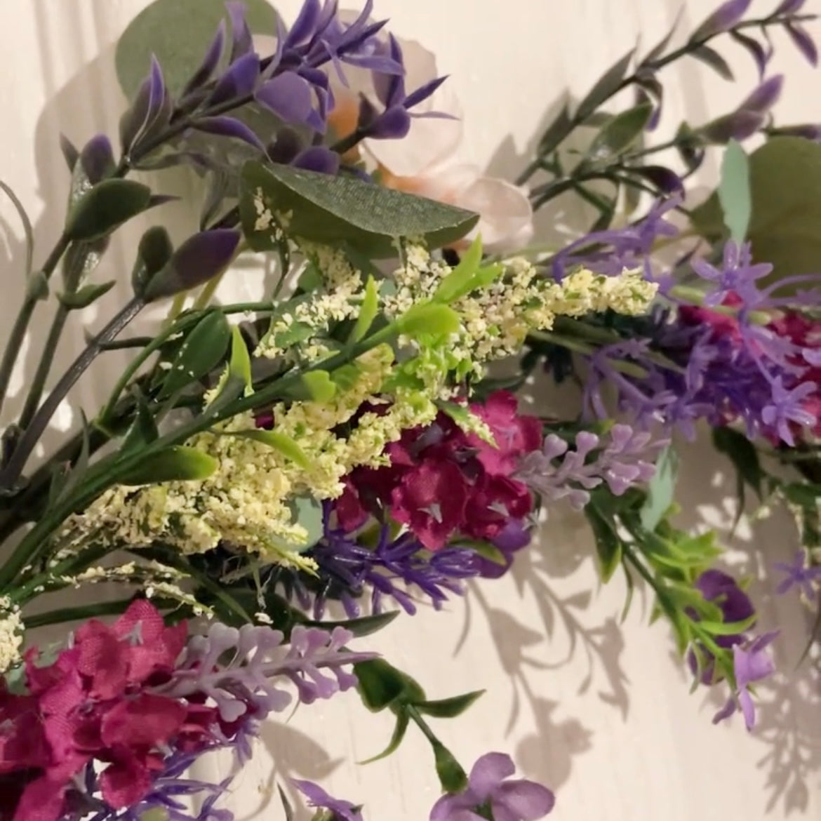 Faux lavender wreath with purple and white blooms, eucalyptus and peach wildflowers, 40 cm diameter styled on a white door.
