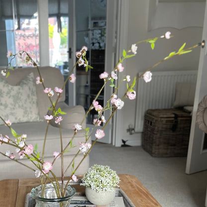 Faux pink blossom spray with three delicate stems styled in a vase on a coffee table.