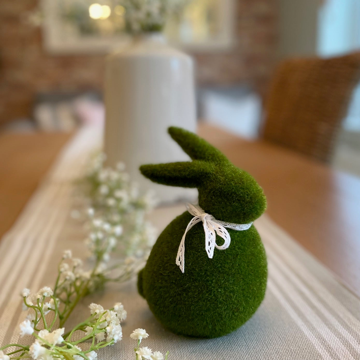 Green faux moss covered bunny decoration on a table with white flowers styled on a table