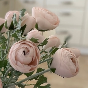 Single faux pastel pink ranunculus stem styled in a rustic stone vase.