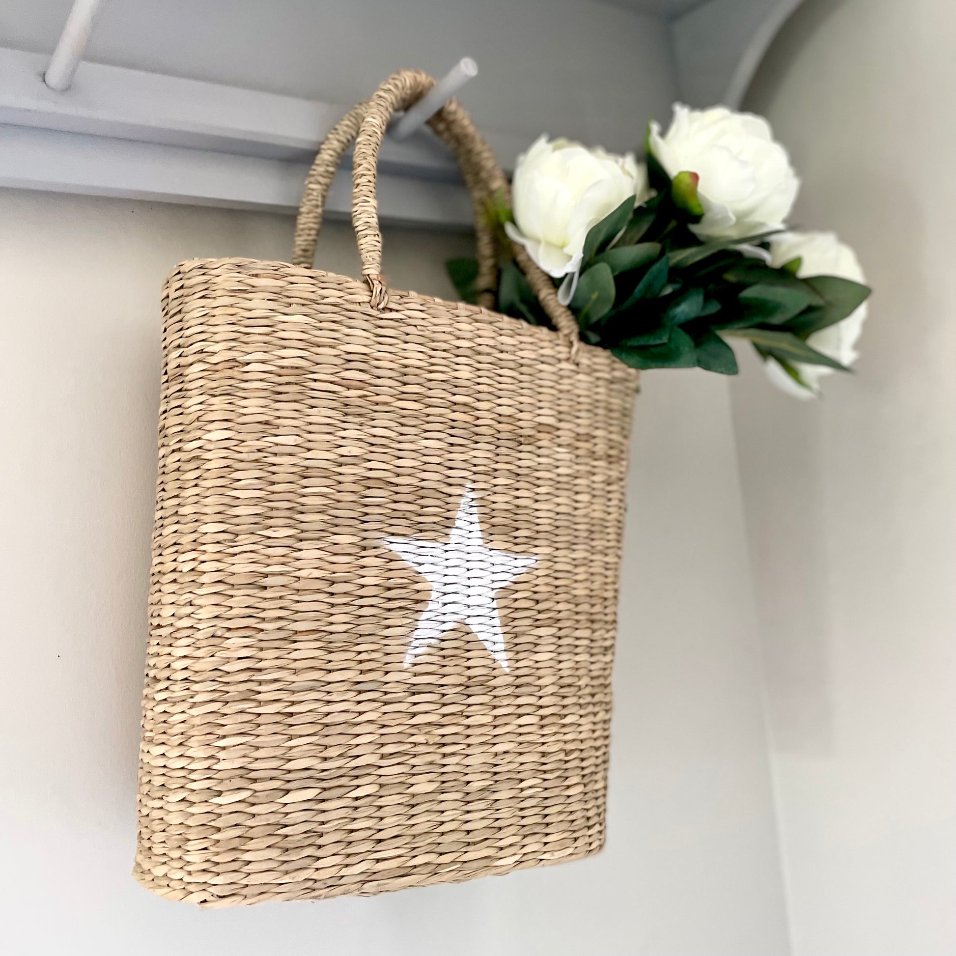 basket of white peony faux stems hanging on a peg shelf.