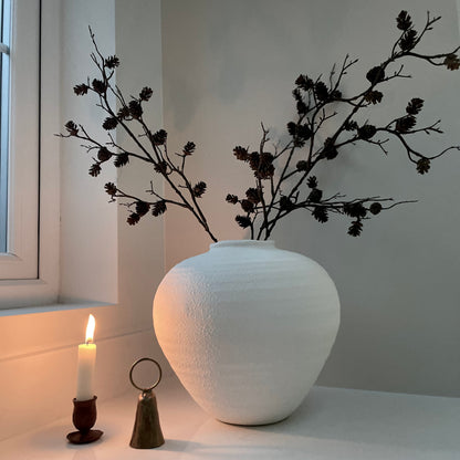faux mini pinecone stem styled in a matte white ceramic vase on a kitchen worktop.