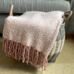 Pink textured throw blanket with fringe draped over a wicker basket on a tiled floor.